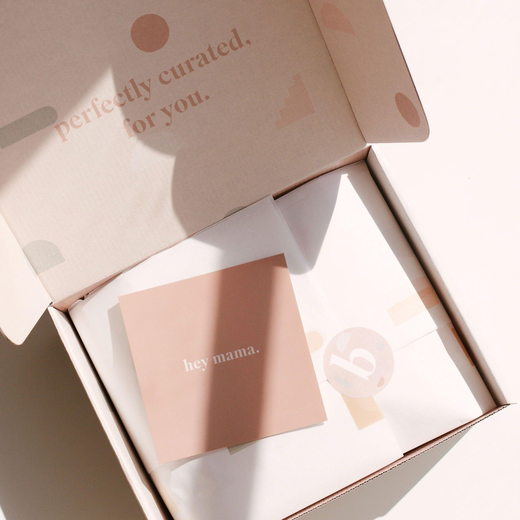 An open package from biglittlethings contains a "hey mama | gift card" along with tissue paper beneath. The inside of the box is branded and includes the phrase "perfectly curated, for you.