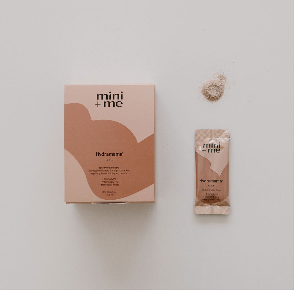 A box and sachet of Mini+Me Hydramama Cola drink mix, an electrolyte-rich hydration beverage, are displayed alongside a small pile of powder against a light background. Ideal for postpartum care or whenever you need to revitalize with refreshing effectiveness.