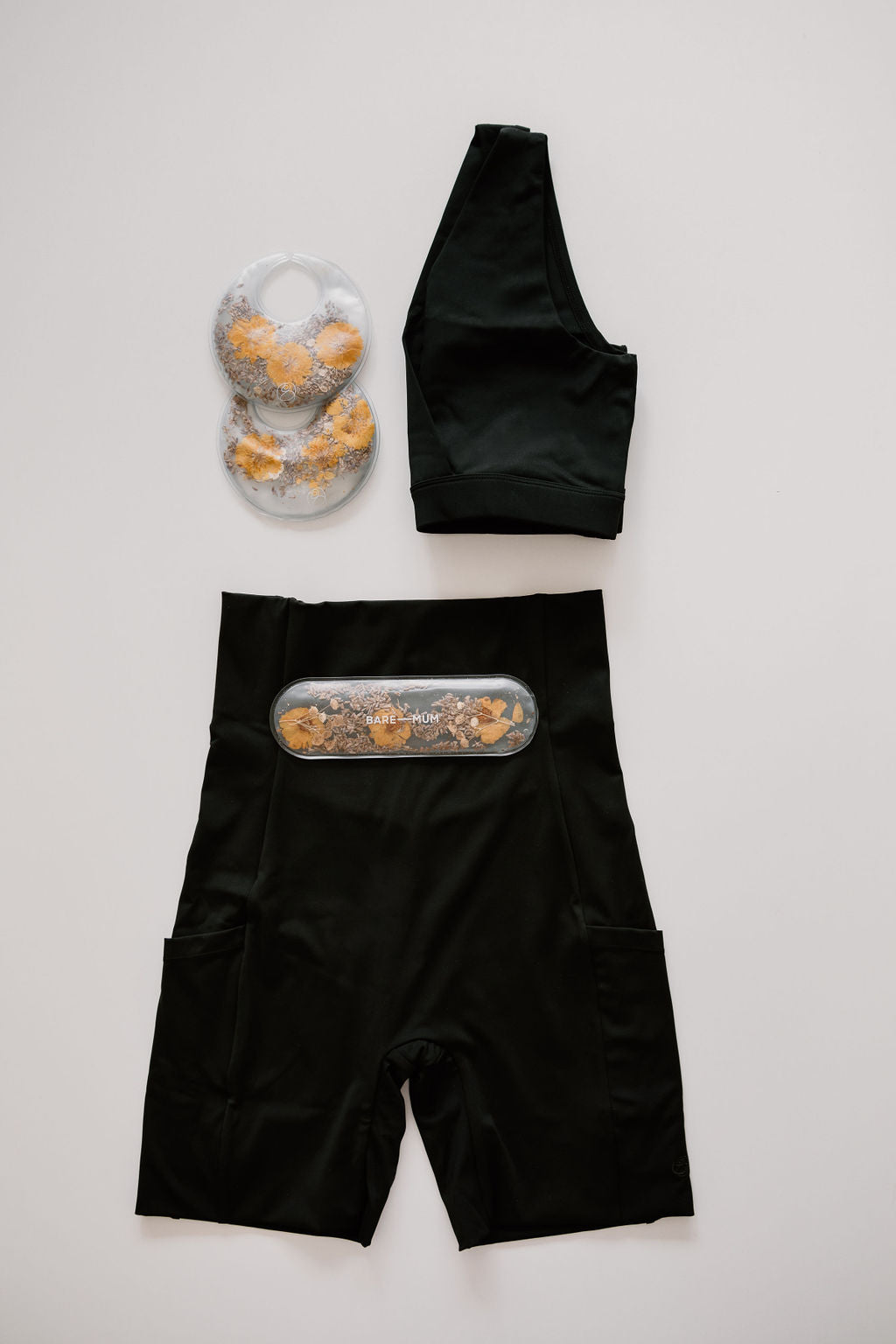 Black athletic crop top and recovery shorts with built-in cooling packs for warm and cool therapy, arranged flat on a light surface. Product Name: bare mum recovery kit. Brand Name: Bare Mum.