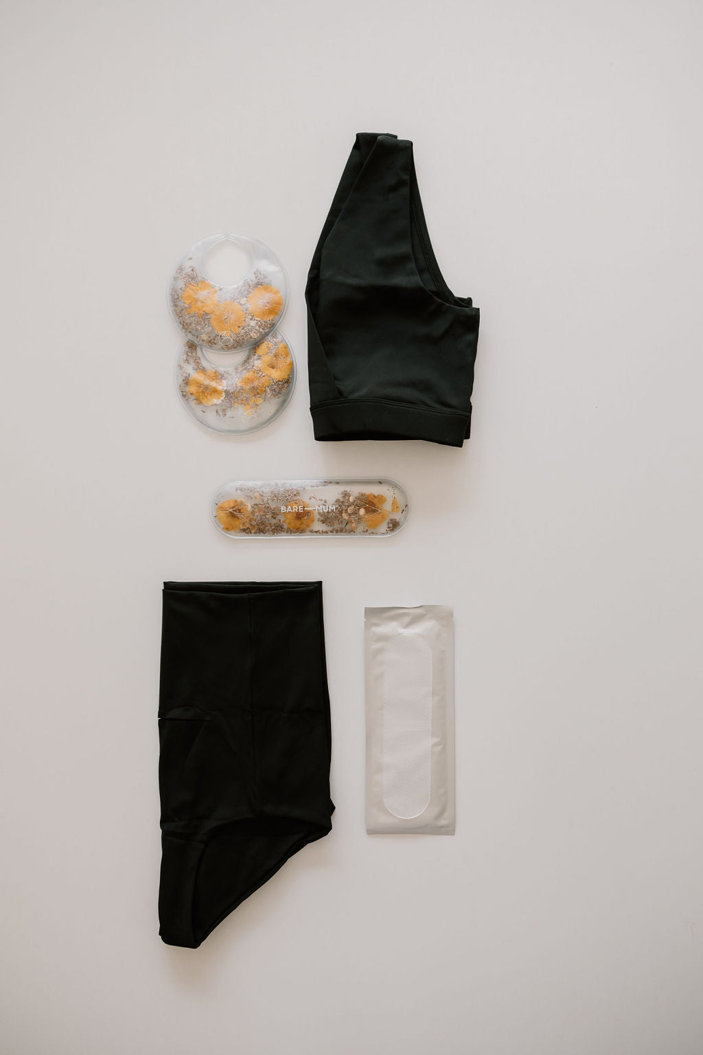 The bare mum recovery kit for c-section by Bare Mum, including an athletic black sports bra and shorts, two ice packs, and a rectangular cooling pack, is laid out forming an ideal postpartum kit for cesarean recovery, all arranged on a white background.